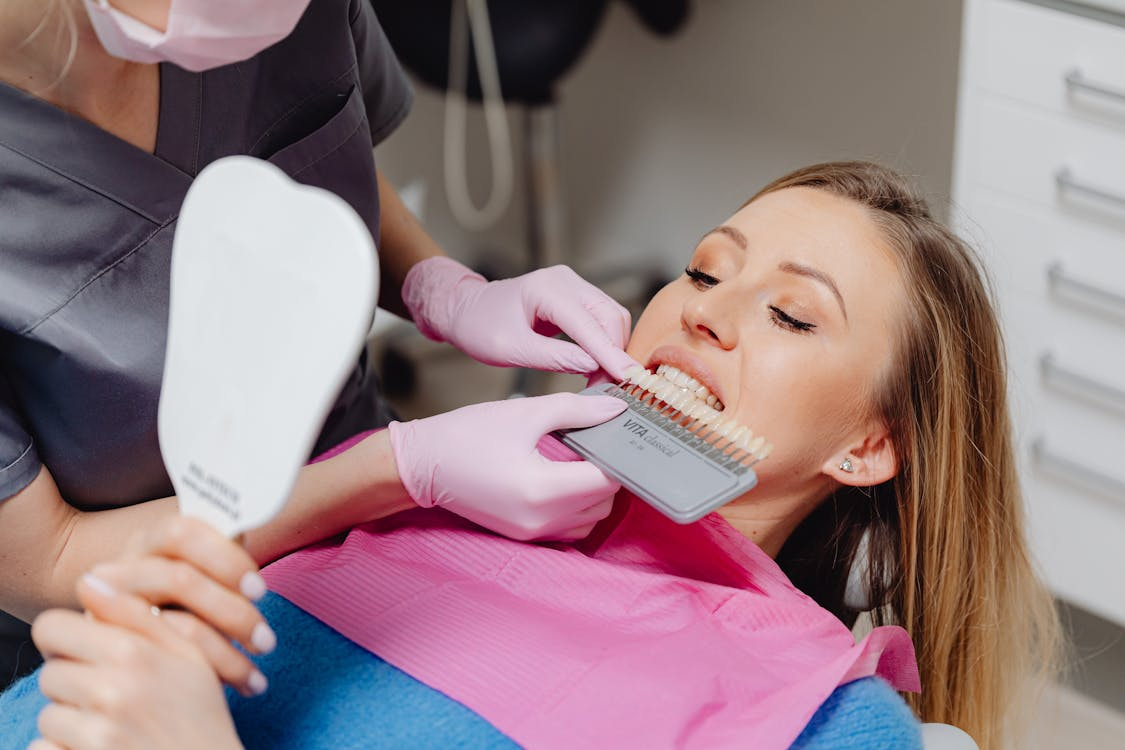 a dentist showing the patient her teeth color using a palette of tooth model with different shades